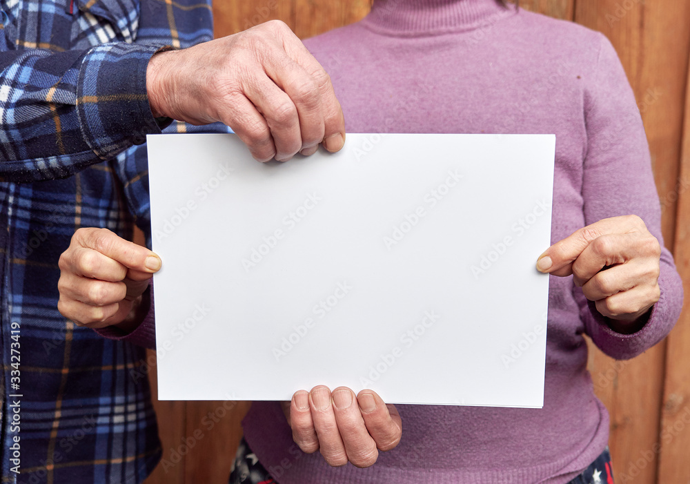 the hands of an old man and old woman hold a white sheet with a text. coronavirus, covid-19. the hands of an old man and old woman hold a white sheet with a text. coronavirus, covid-19.