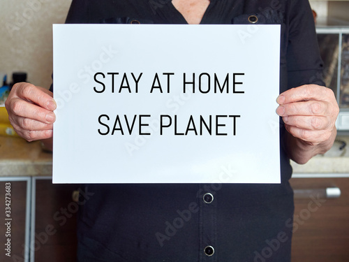 the hands of an old woman hold a white sheet with the text: stay at home, save planet. coronavirus, covid-19.
