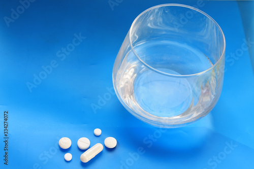  white pills and a glass of water stands on a table on a blue background