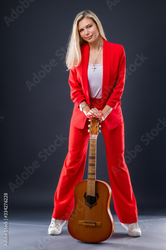Expressive young woman in a bright red suit with a guitar on stage