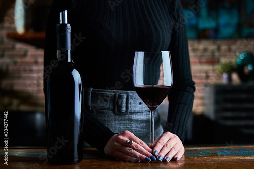 Woman in black shirt and grey skirt tasting red wine. Close up image of woman holding wine glass and wine bottle. photo