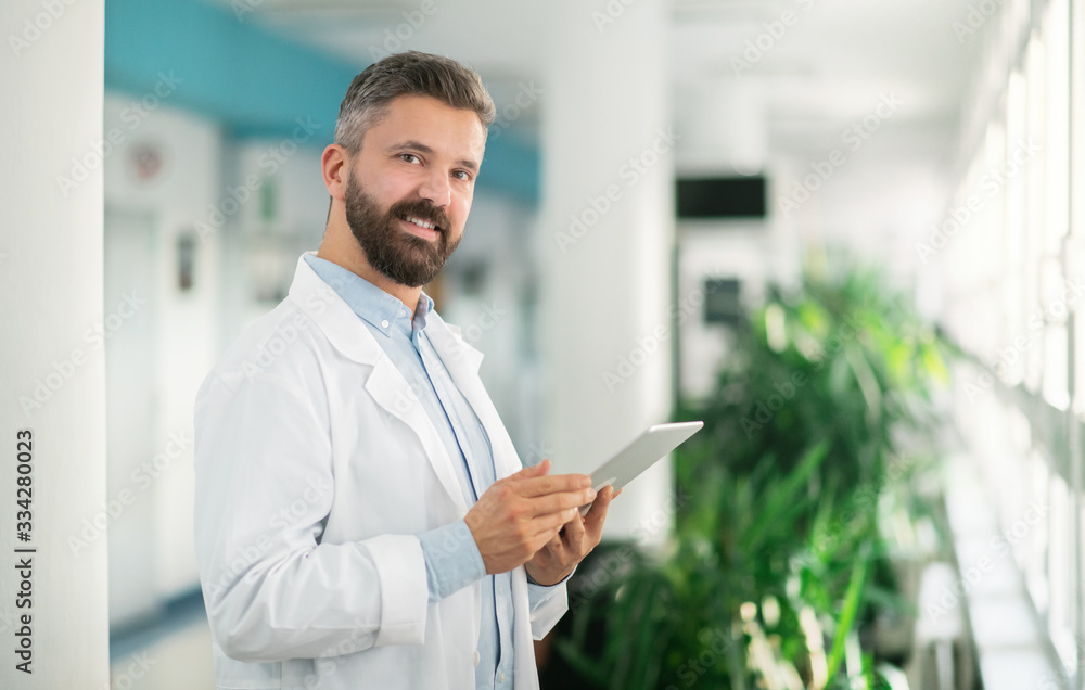 Portrait of man doctor standing in hospital, using tablet. Portrait of man doctor standing in hospital, using tablet.