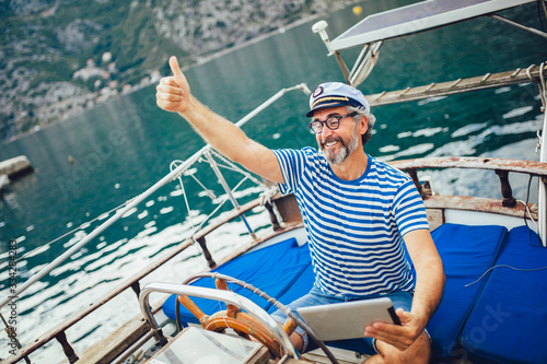 Mature man standing on the deck of his boat and using digital tablet on a sunny afternoon. © Mediteraneo