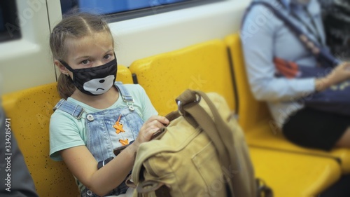 Little girl travel caucasian ride at overground train airtrain with wearing protective medical red mask. Child baby tourist at airtrain with respirator. Pandemic Coronavirus covid-19. People in mask. photo