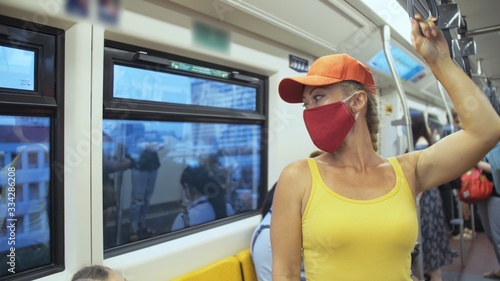 Woman travel caucasian ride at overground train airtrain with wearing protective medical red mask. Girl tourist at airtrain with respirator. Pandemic virus Coronavirus covid-19. People in mask. photo