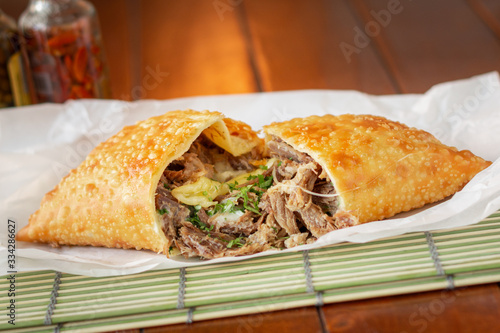 Pastel frito Brasileiro de contra filé bovino e queijo encima de esteira e guardanapo com fundo desfocado e molho de pimenta  