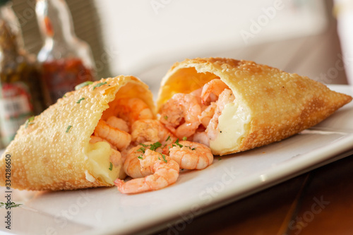 Pastel da culinária brasileira de camarão e requeijão bem recheado  encima de prato branco de louça 
