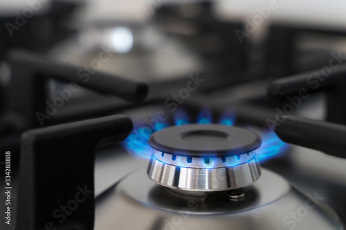 Closeup blue flame from a gas stove burner. Stainless steel kitchen surface with cast-iron grill.