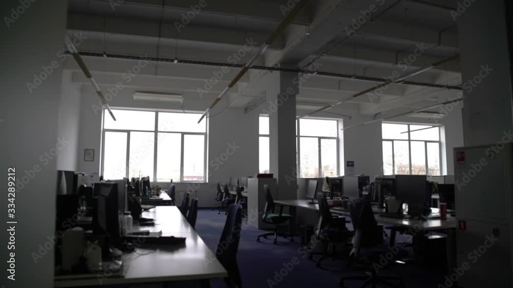 Pan shot of empty open space office with modern and comfortable workplaces. There are desks with laptop, tablet, computers and stationery on them