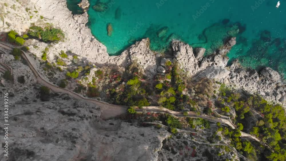 Aerial drone top view tracking shot of huge number of luxury boats berth over crystal clear seawater in Capri Italy near rock cliffs with colorful trees Aerial drone top view tracking shot of huge number of luxury boats berth over crystal clear seawater in Capri Italy near rock cliffs with colorful trees