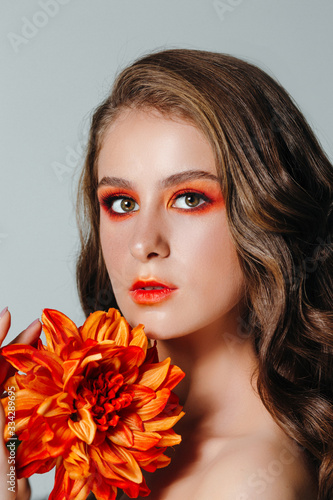 Beauty portrait of a woman with an orange gerbera flower and bright makeup. Autumn girl. Miss September.