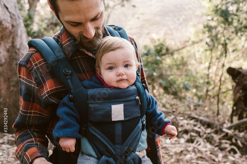 father carrying his baby daughter and taking photos on a hike in the woods