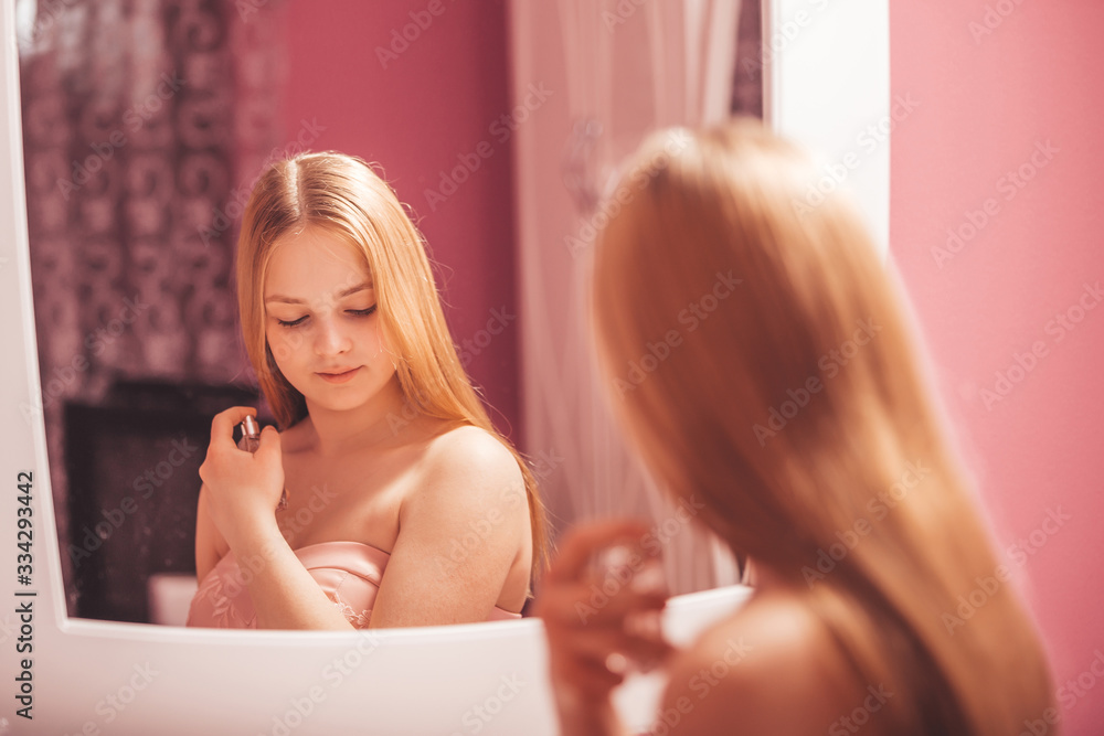 Obraz premium Teenage girl in a dress holding a perfume bottle and applying it
