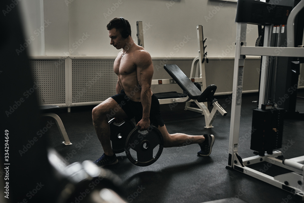 Muscular athlete man with a naked torso in headphones on workout in the gym, pumps his body and listens to music Muscular athlete man with a naked torso in headphones on workout in the gym, pumps his body and listens to music