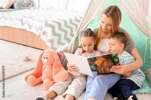 Photos Nanny and cute little children reading book at home