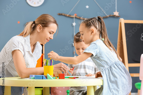 Φωτογραφία Nanny with cute little children playing and drawing at home