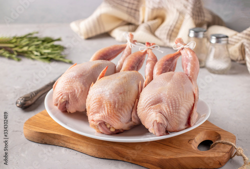 Three raw fresh quails on a white plate on a wooden board, Closeup, gray background