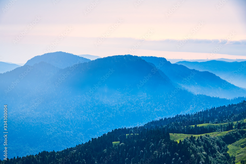 Green mountain slope. Layers of mountains in the haze during sunset. Krasnaya Polyana, Sochi, Caucasus, Russia.