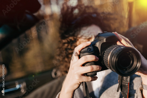 curly woman photographer in a convertible car rides on a sunny day on the road and rejoices in sunglasses.