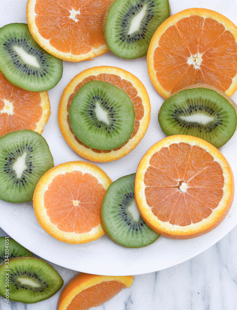 Close up of sliced oranges and kiwi on a white plate on a marble background. Close up of sliced oranges and kiwi on a white plate on a marble background.