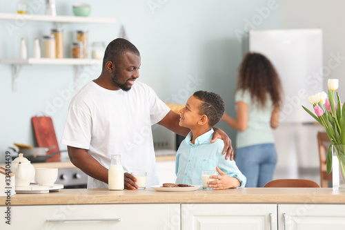 African-American man and his son drinking milk in kitchen