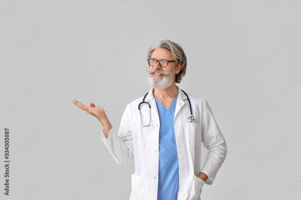 Portrait of senior male doctor showing something on grey background Portrait of senior male doctor showing something on grey background