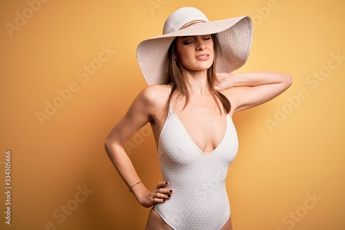 Young beautiful brunette woman on vacation wearing swimsuit and summer hat Suffering of neck ache injury, touching neck with hand, muscular pain