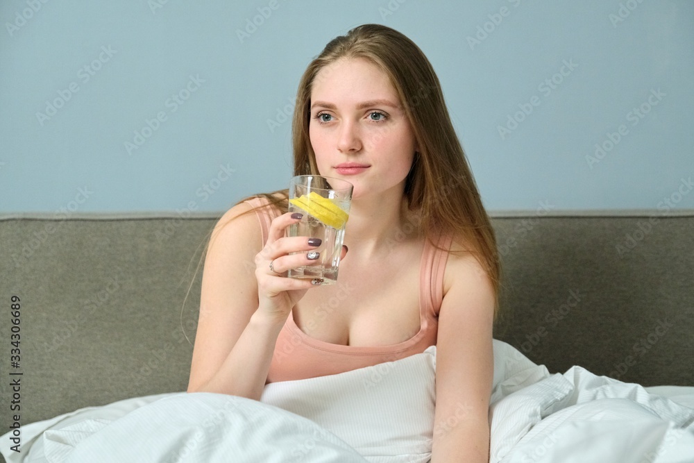 Young woman in bed with morning glass of water with lemon