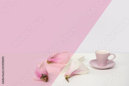 cup of cappuccino on a white table, blooming magnolia buds, a book in a white cover on a delicate pink background, a blank for the designer, an invitation form, a spring mood concept