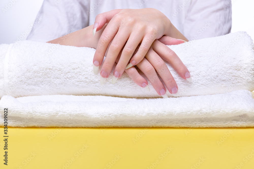 Beautiful hands of young woman close-up on towel. Spa treatments for nails. Space for text. Woman holds hands on towel for manicure treatment procedure in spa salon.
