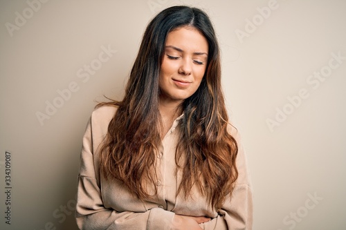 Young beautiful brunette woman wearing casual shirt standing over white background with hand on stomach because indigestion, painful illness feeling unwell. Ache concept.