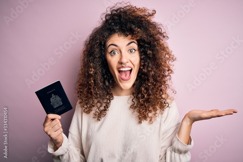 Beautiful tourist woman with curly hair and piercing holding canada canadian passport id very happy and excited, winner expression celebrating victory screaming with big smile and raised hands
