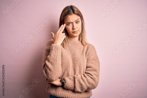 Young beautiful blonde woman wearing winter wool sweater over pink isolated background Shooting and killing oneself pointing hand and fingers to head like gun, suicide gesture. © Krakenimages.com