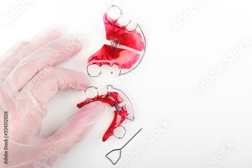 An orthodontist wearing disposable gloves picks up an orthodontic appliance for children on a white table at the dentist's office. Concept of oral health in childhood. Space for text.