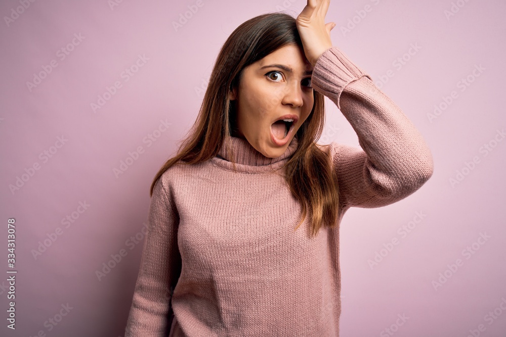Beautiful young woman wearing turtleneck sweater over pink isolated background surprised with hand on head for mistake, remember error. Forgot, bad memory concept. Beautiful young woman wearing turtleneck sweater over pink isolated background surprised with hand on head for mistake, remember error. Forgot, bad memory concept.