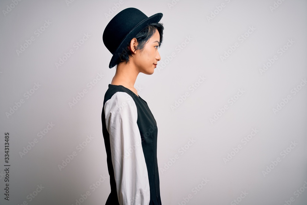Young beautiful asian girl wearing casual dress and hat standing over isolated white background looking to side, relax profile pose with natural face with confident smile. Young beautiful asian girl wearing casual dress and hat standing over isolated white background looking to side, relax profile pose with natural face with confident smile.