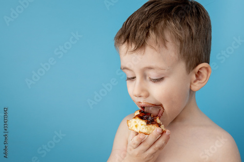 Little boy eating donut chocolate on blue background. Cute happy boy smeared with chocolate around his mouth. Child concept, tasty food for kids © volody10