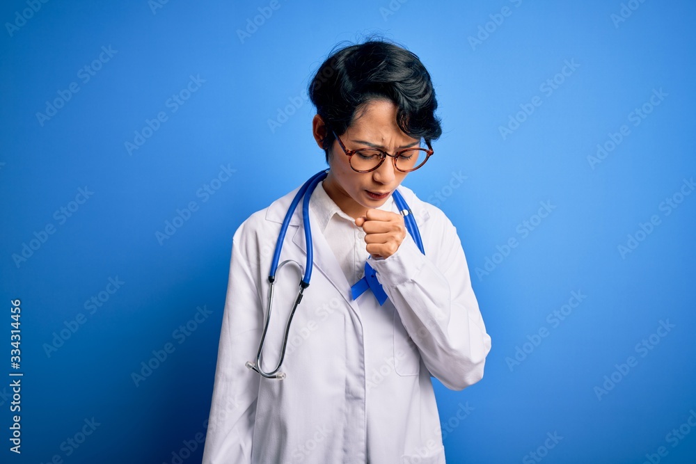 Young beautiful asian doctor girl wearing stethoscope and coat with blue cancer ribbon feeling unwell and coughing as symptom for cold or bronchitis. Health care concept. Young beautiful asian doctor girl wearing stethoscope and coat with blue cancer ribbon feeling unwell and coughing as symptom for cold or bronchitis. Health care concept.