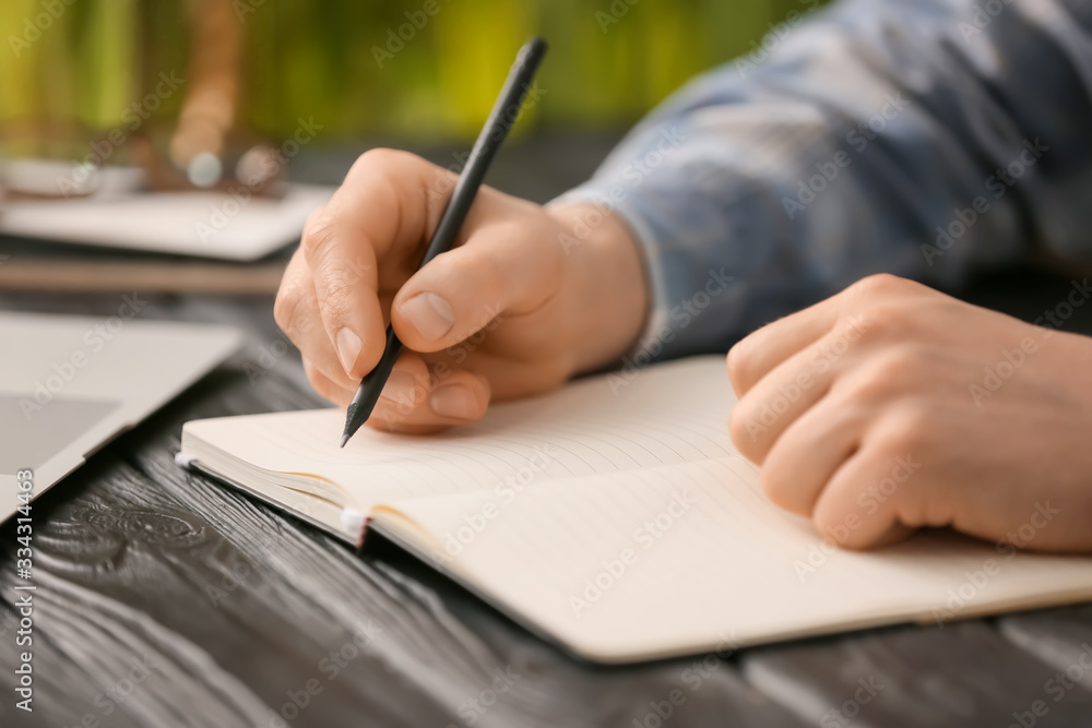 Man writing something in notebook at table Man writing something in notebook at table