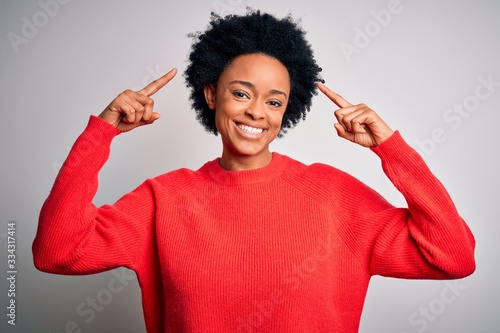 Young beautiful African American afro woman with curly hair wearing red casual sweater smiling pointing to head with both hands finger, great idea or thought, good memory