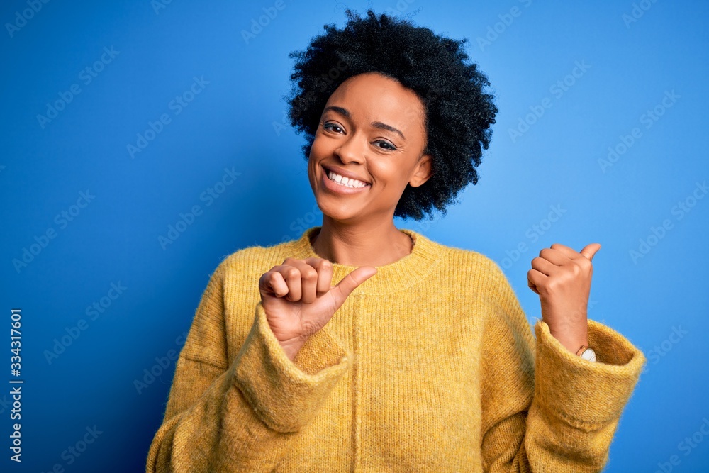 Young beautiful African American afro woman with curly hair wearing yellow casual sweater Pointing to the back behind with hand and thumbs up, smiling confident Young beautiful African American afro woman with curly hair wearing yellow casual sweater Pointing to the back behind with hand and thumbs up, smiling confident