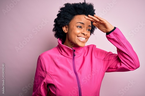 Young African American afro sportswoman with curly hair wearing sportswear doin sport very happy and smiling looking far away with hand over head. Searching concept. photo