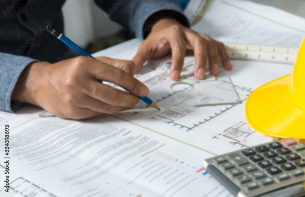 Young man working on blueprint with engineering tools and safety helmet calculator on desk. Construction concept. Young man working on blueprint with engineering tools and safety helmet calculator on desk. Construction concept.