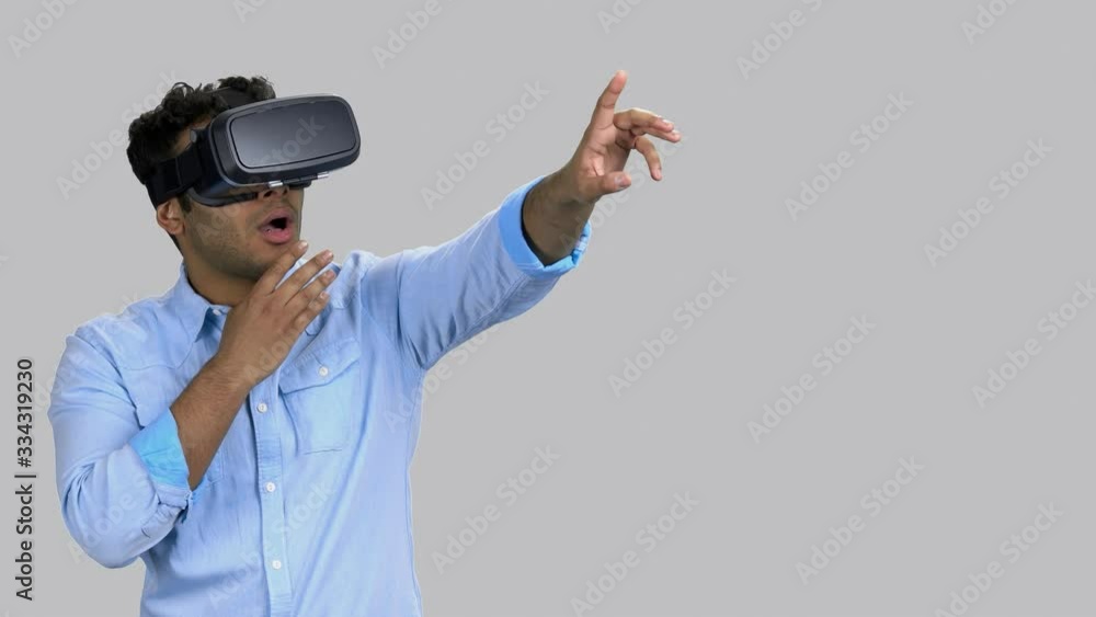 Amazed and shocked dark-skinned young man wearing vr-headset. Expressive emotional guy. Grey background. Amazed and shocked dark-skinned young man wearing vr-headset. Expressive emotional guy. Grey background.