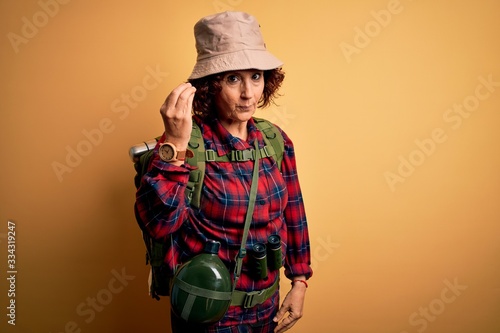 Middle age curly hair hiker woman hiking wearing backpack and water canteen using binoculars Doing Italian gesture with hand and fingers confident expression
