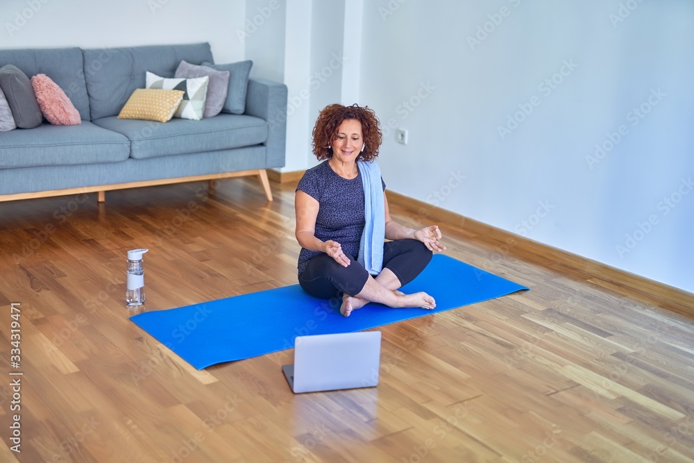 Middle age beautiful sportswoman smilig happy. Sitting on mat with smile on face using laptop at home