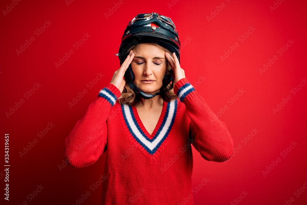 Fototapeta premium Middle age beautiful blonde motorcyclist woman wearing moto helmet over red background suffering from headache desperate and stressed because pain and migraine. Hands on head.