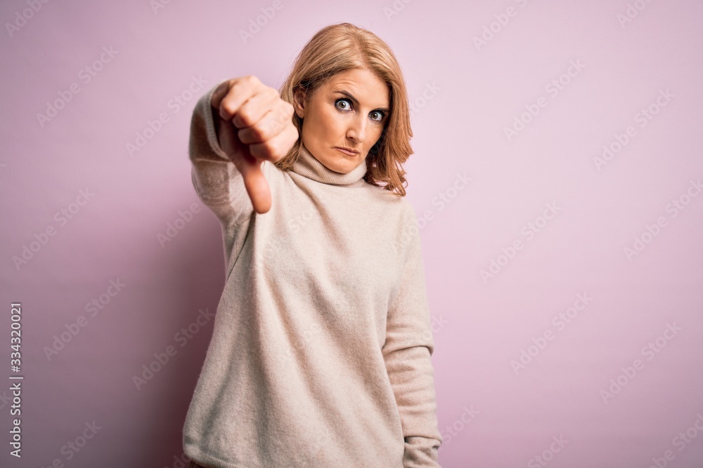 Middle age beautiful blonde woman wearing casual turtleneck sweater over pink background looking unhappy and angry showing rejection and negative with thumbs down gesture. Bad expression. Middle age beautiful blonde woman wearing casual turtleneck sweater over pink background looking unhappy and angry showing rejection and negative with thumbs down gesture. Bad expression.