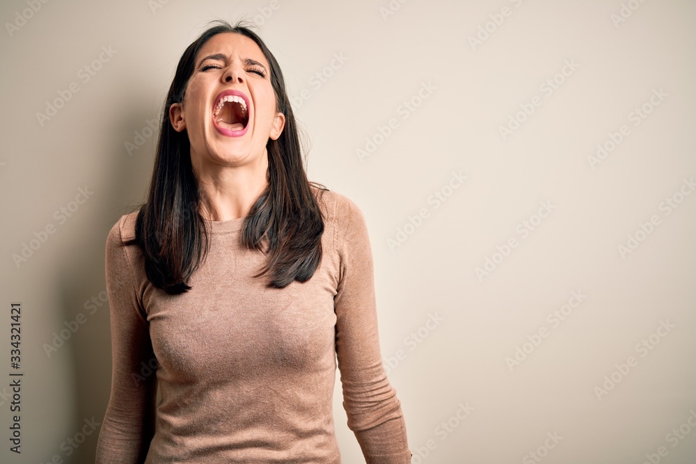 Young brunette woman with blue eyes wearing casual sweater over isolated white background angry and mad screaming frustrated and furious, shouting with anger. Rage and aggressive concept. Young brunette woman with blue eyes wearing casual sweater over isolated white background angry and mad screaming frustrated and furious, shouting with anger. Rage and aggressive concept.