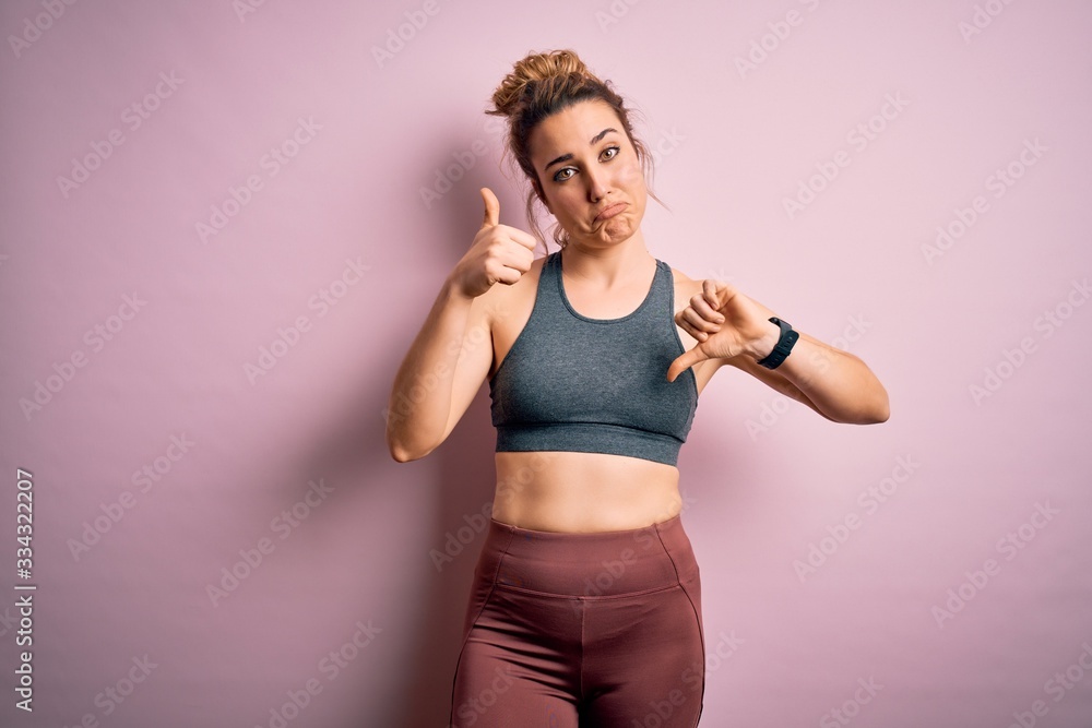 Young beautiful blonde sportswoman doing sport wearing sportswear over pink background Doing thumbs up and down, disagreement and agreement expression. Crazy conflict Young beautiful blonde sportswoman doing sport wearing sportswear over pink background Doing thumbs up and down, disagreement and agreement expression. Crazy conflict